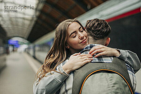 Lächelnde Frau umarmt ihren Freund am Bahnhof