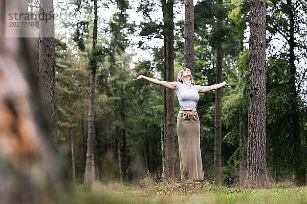 Young woman standing with arms outstretched in front of trees at forest