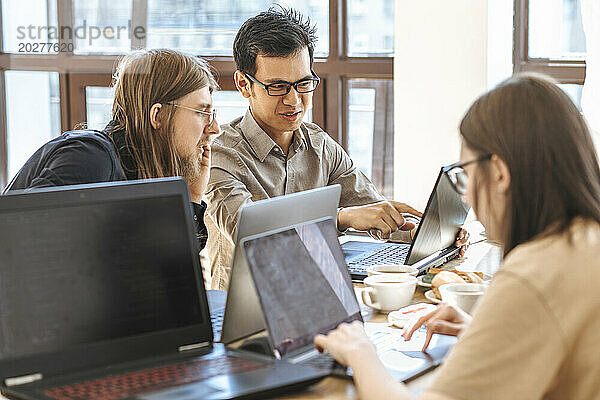 Programmierer diskutieren am Laptop neben einer Geschäftsfrau  die beim Start arbeitet