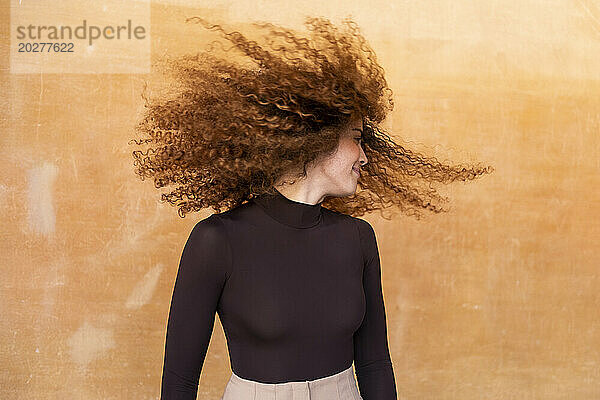 Verspielte Frau wirft Haare vor braunem Hintergrund