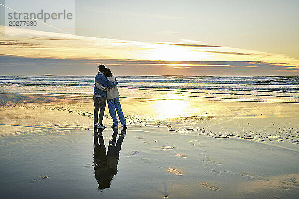 Junge Frau und Mann umarmen sich und genießen den Meerblick am Strand