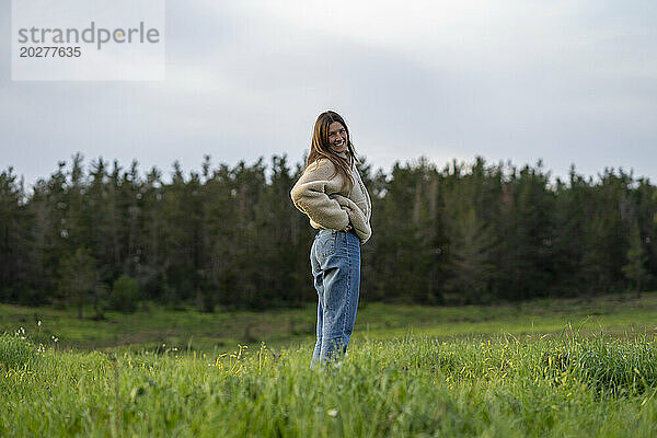 Glückliche junge Frau steht auf Gras auf der Wiese