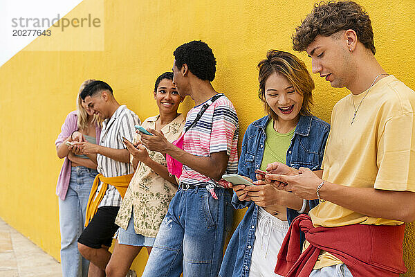 Eine Gruppe von Freunden lehnt mit ihren Smartphones an einer gelben Wand
