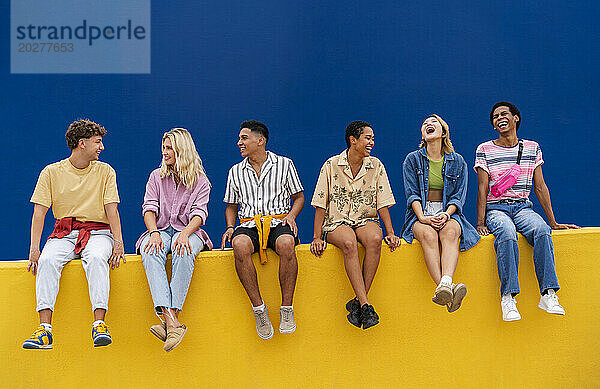 Happy friends with colorful clothing sitting on yellow wall together