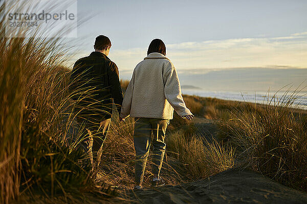 Junges Paar hält Händchen und geht am Strand spazieren
