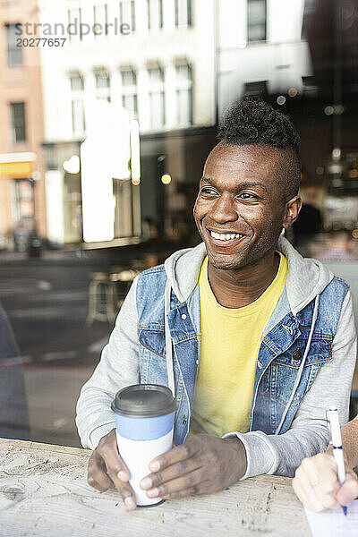 Lächelnder Mann  der im Café aus dem Fenster schaut