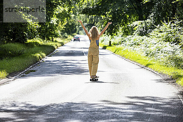 Junge Frau mit erhobenen Armen beim Skateboarden im Wald