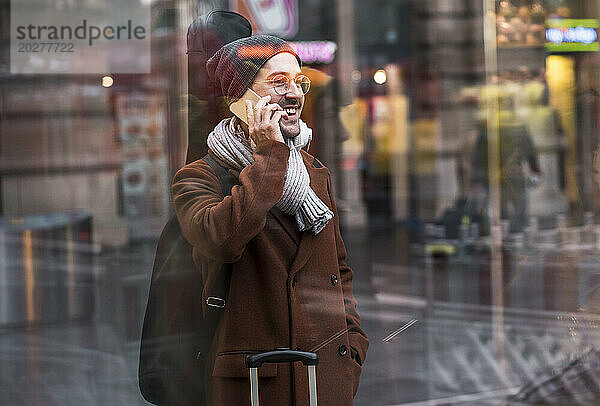 Glücklicher Mann  der einen langen Mantel trägt und mit dem Smartphone spricht