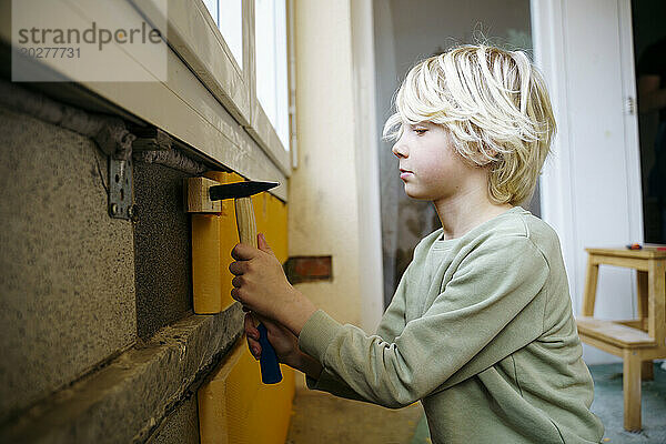 Junge hämmert Holzstück an Wand in Zimmer  das gerade renoviert wird