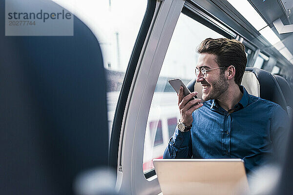 Glücklicher Geschäftsmann  der im Zug auf dem Smartphone spricht