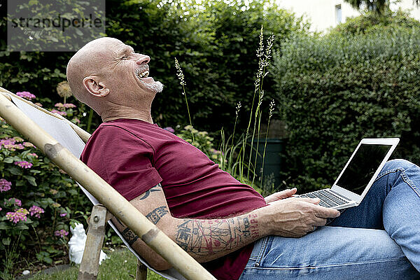 Fröhlicher Freiberufler sitzt mit Laptop im Garten