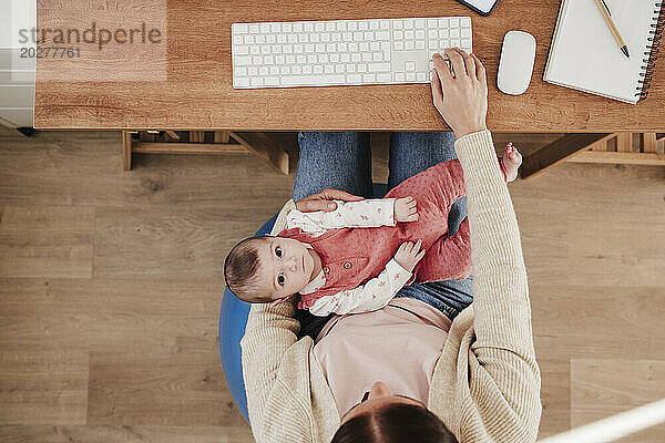 Cute baby girl lying on working mother's lap in home office