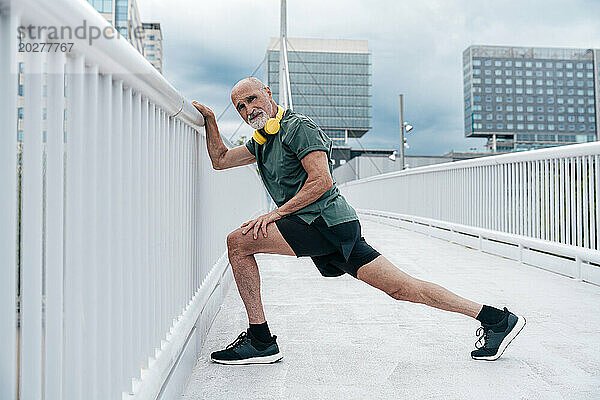 Aktiver älterer Mann übt Ausfallschrittübungen auf Fußgängerbrücke in der Stadt