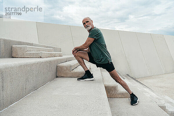 Selbstbewusster  aktiver älterer Mann  der sich auf Stufen streckt