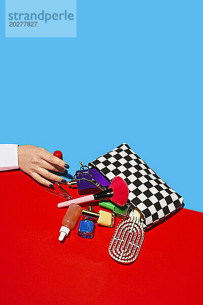 Studio shot of female hand touching cosmetics falling out of checked purse