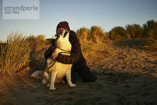 Junge Frau umarmt Husky-Hund auf Sand