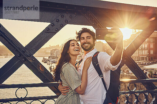 Lächelndes Paar macht ein Selfie mit dem Smartphone an der Dom-Luis-Brücke  Porto  Portugal