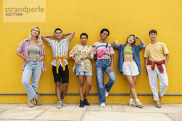 Sorglose Freunde in farbenfroher Kleidung lehnen an einer gelben Wand