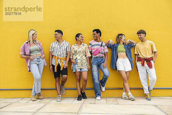 Sorglose Freunde in farbenfroher Kleidung unterhalten sich vor einer gelben Wand