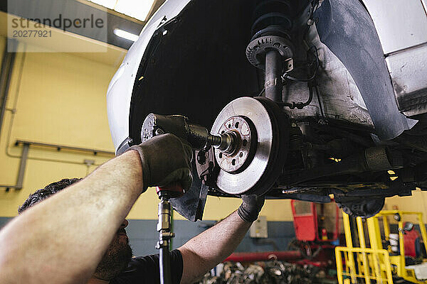 Mechanic using impact wrench to disassemble vehicle parts at workshop