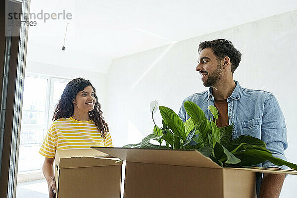 Happy couple carrying cardboard boxes at new home