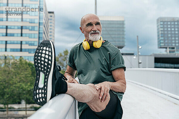 Rentner streckt Bein auf Geländer an Fußgängerbrücke in der Stadt