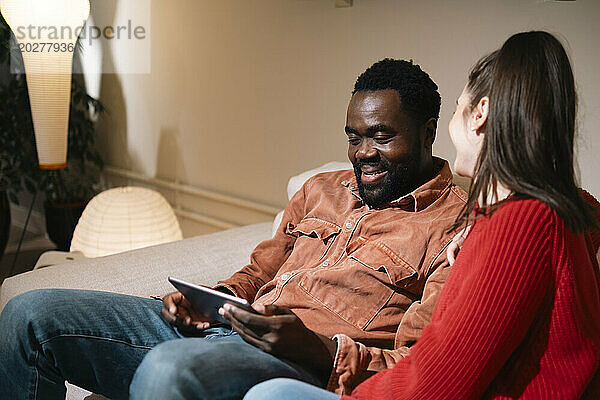 Glücklicher Mann sitzt mit Frau auf Sofa und nutzt Tablet-PC zu Hause