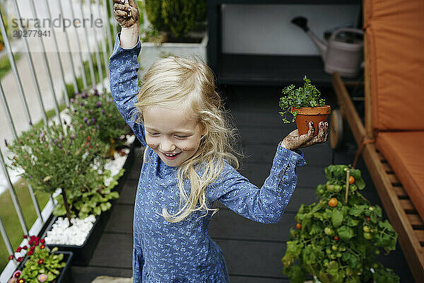 Fröhliches Mädchen hält Pflanze im Balkongarten