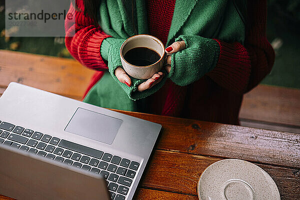 Freiberufler hält Kaffeetasse neben Laptop im Café