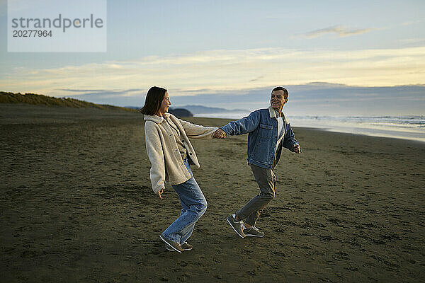 Smiling man holding hand of girlfriend and walking on beach