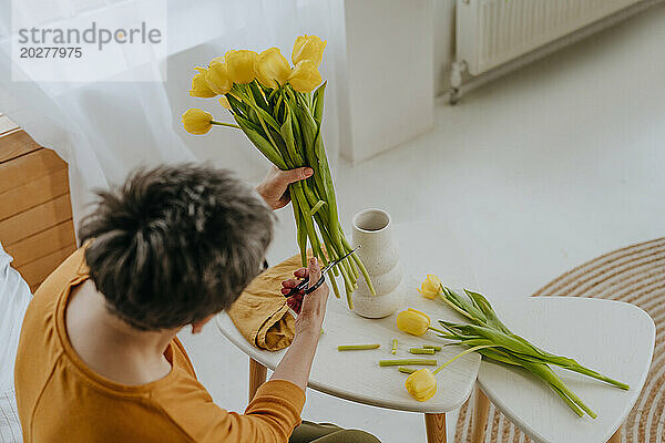 Reife Frau schneidet zu Hause Tulpenstiele