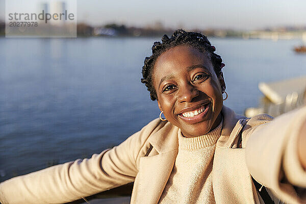 Glückliche Frau  die bei Sonnenuntergang ein Selfie in der Nähe des Flusses macht