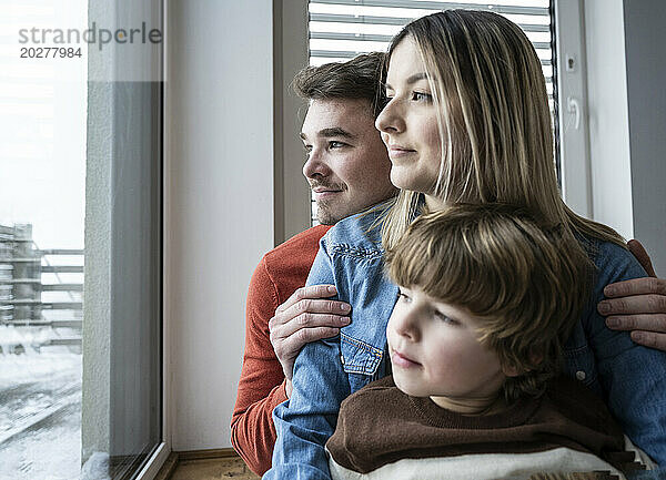 Lächelnder Vater und Mutter mit Sohn  die zu Hause durch das Fenster schauen