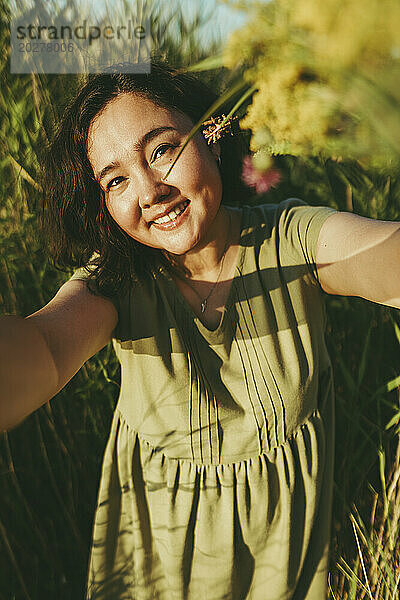 Lächelnde reife Frau macht ein Selfie inmitten von Gras im Feld