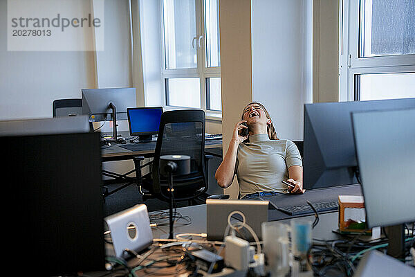 Fröhliche junge Frau  die im Büro mit dem Smartphone spricht