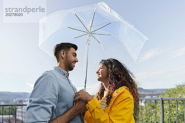 Romantisches Paar steht unter einem Sonnenschirm auf dem Balkon