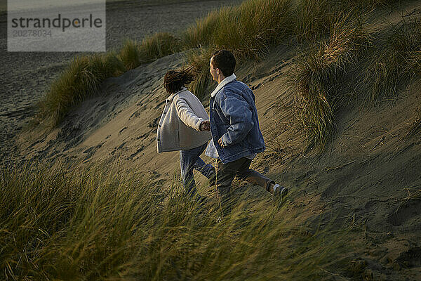 Young couple holding hands and running on ocean beach