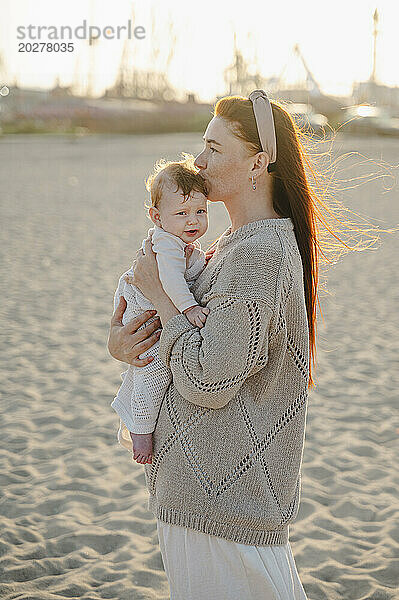 Frau hält und küsst kleines Mädchen am Strand