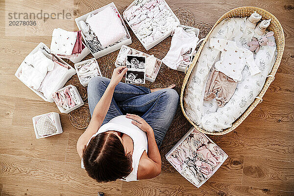Pregnant woman holding ultrasound photographs near moses basket at home