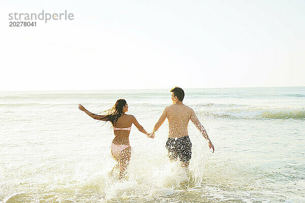 Sorgloses Paar hält Händchen und läuft am Strand im Wasser