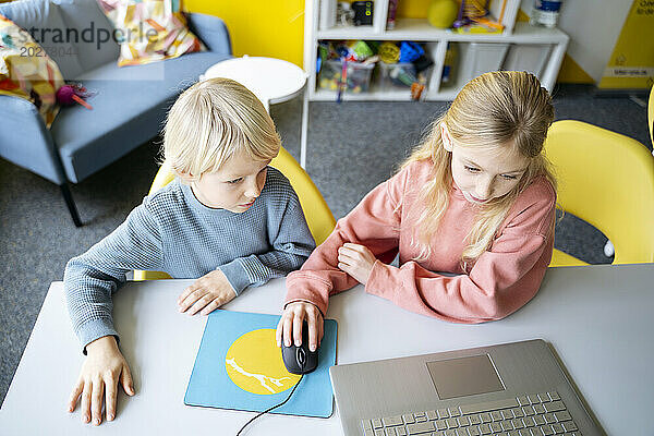 Mädchen und Junge teilen sich einen Laptop  um im Klassenzimmer Computerprogrammierung zu lernen