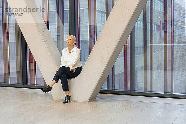 Ältere Geschäftsfrau sitzt inmitten einer architektonischen Säule