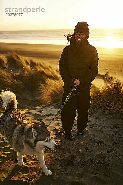 Glückliche junge Frau  die am Strand mit einem Husky-Hund spazieren geht