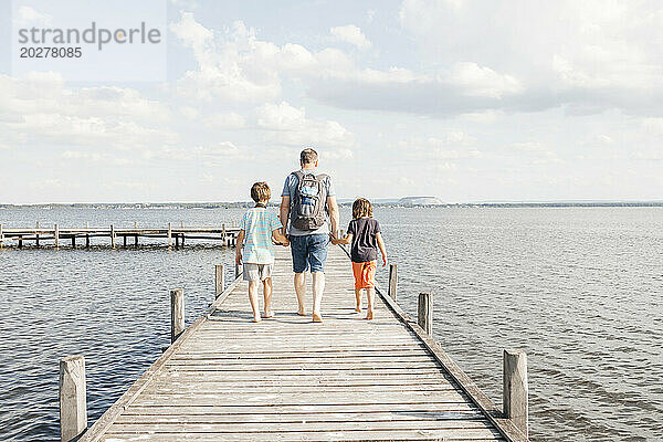 Vater geht mit Söhnen auf Holzsteg am See spazieren