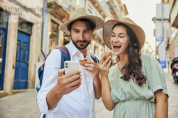 Glückliches Paar macht ein Selfie mit dem traditionellen Dessert Pastel de Nata über das Smartphone