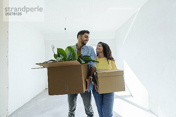 Happy young couple carrying cardboard boxes in room under renovation