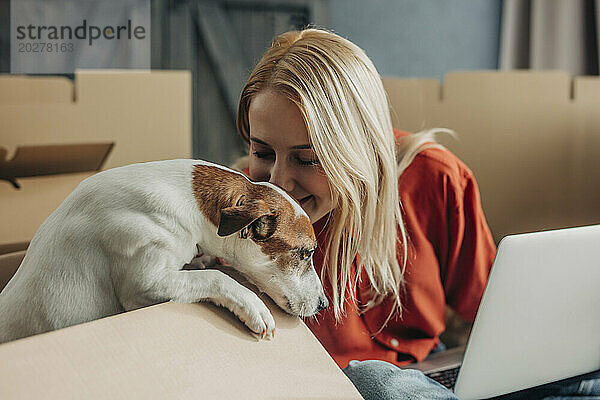 Lächelnde Frau küsst Hund und sitzt mit Laptop