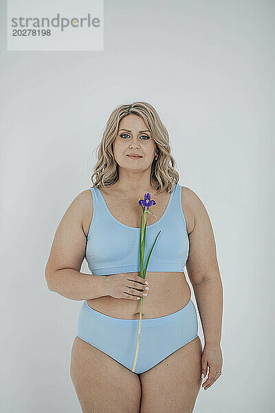 Plus size woman in lingerie holding flower against white background