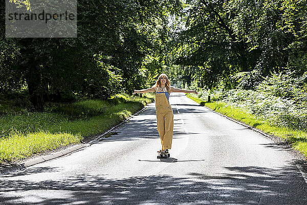 Young woman with arms outstretched skateboarding in forest