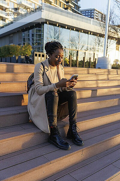 Frau sitzt auf Treppen und benutzt Smartphone in der Stadt